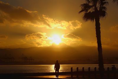 Silhouette man standing by sea against sky during sunset