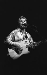 Young man playing guitar against black background