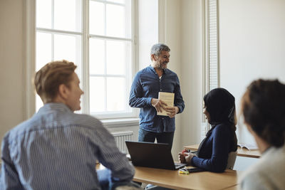 Smiling male professor with book standing in classroom