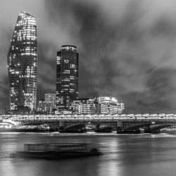 Illuminated buildings by river against sky in city at night