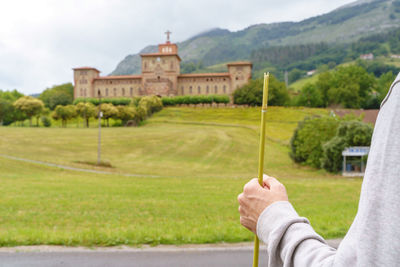 Person holding umbrella by building against sky