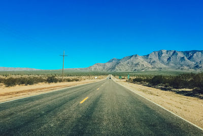 Road by mountains against clear blue sky