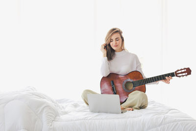 Full length of a young woman sitting on bed