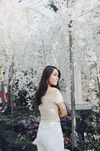 Rear view of smiling young woman standing against plants in park