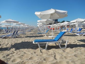 Deck chairs on beach against blue sky