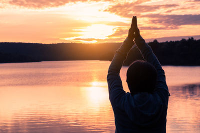 Midsection of woman practicing yoga by lake during sunset