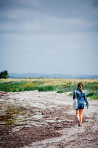 Rear view of woman walking on field against sky