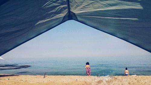 Rear view of friends standing on shore seen through tent