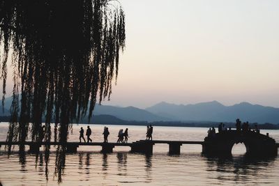 Silhouette people on lake against sky during sunset