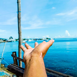 Cropped image of hand against sea against sky