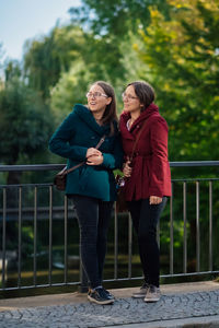 Sisters looking away while standing by railing in city