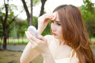 Woman applying powder compact on face against trees