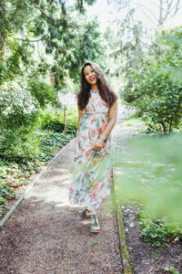 Happy multiracial japanese woman in romantic floral maxi dress in summer park