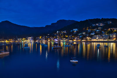 Sailboats moored in illuminated city against sky at dusk