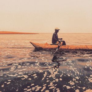 Side view of man sitting on boat in sea against sky