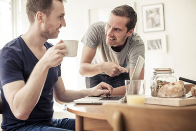 Homosexual couple using laptop together at breakfast table in home