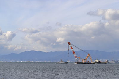 Cranes at commercial dock by sea against sky