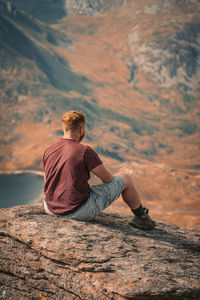 Rear view of man sitting on rock