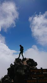 Low angle view of woman standing on rock against sky