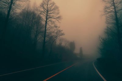 Road by trees against sky during sunset