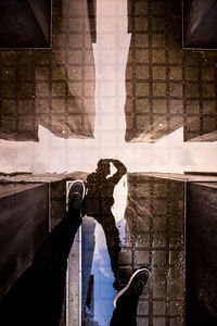 Reflection of man photographing while standing by puddle