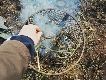 Cropped image of hand putting sticks in fire