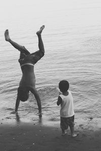 Boy looking at brother doing handstand on sea shore at beach