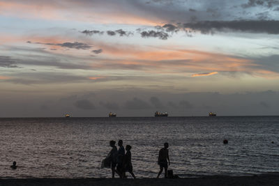 Silhouette people on beach against sky during sunset