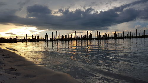 Wooden posts on beach against sky during sunset