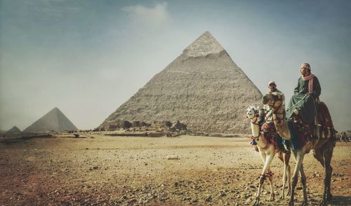 Men sitting on camel against great pyramid of giza
