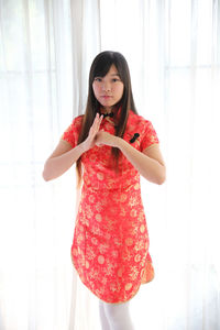 Portrait of young woman standing against curtain