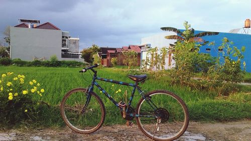 Bicycle on field by house against sky