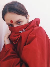 Portrait of woman covering her face in red jacket against white wall