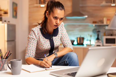 Side view of young woman using laptop while sitting on table