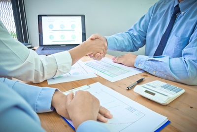 Midsection of businessman shaking hands with colleague in office