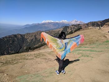 Rear view of woman standing with sarong at mountain peak looking at sky