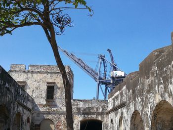 Low angle view of crane by building against clear blue sky