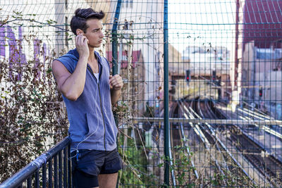 Side view of young woman standing by fence