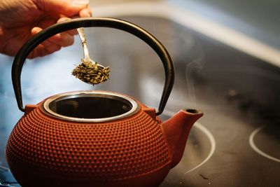 Cropped image of person adding herbs in tea kettle