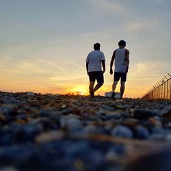 Rear view of friends standing on pebbles at sunset