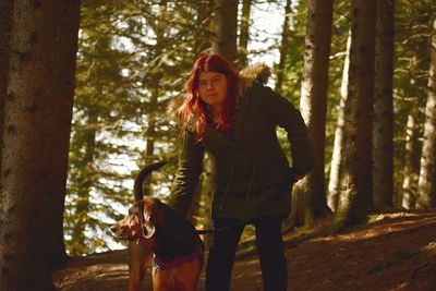 Portrait of woman with dog standing on land in forest