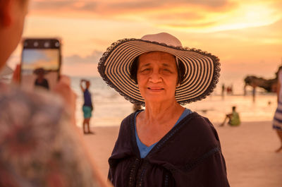 Portrait of woman wearing hat at beach against sky during sunset