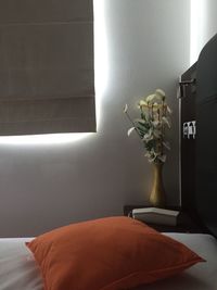 Orange pillow on bed against flower vase