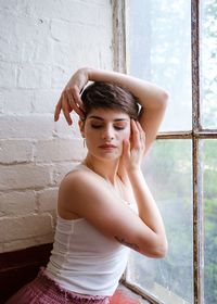 Young woman looking down while standing against window