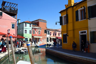 People in canal by buildings against sky in city