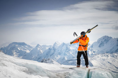 Portrait of a young skier with skis on his shoulder. it stands high in the mountains on a glacier