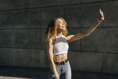 Young woman doing selfie standing by wall outdoors