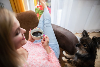 The girl sits with a cup of coffee and the pie looks on with interest.