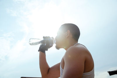 Full length of shirtless man holding camera against sky