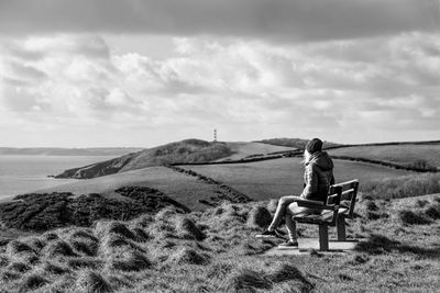 Rear view of woman sitting on sand against sky